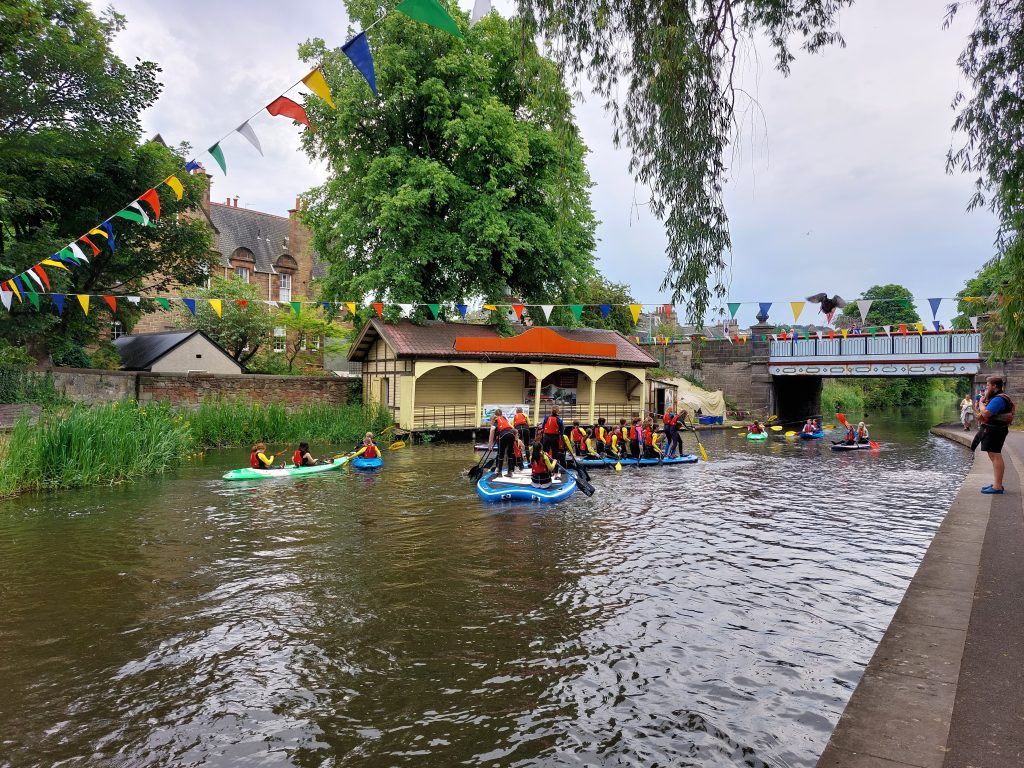 Canal Day 2023 image. Shows people having fun on paddle boards and in canoes or kayaks on the Edinburgh Union Canal.